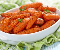 a white bowl filled with carrots on top of a green cloth next to a napkin