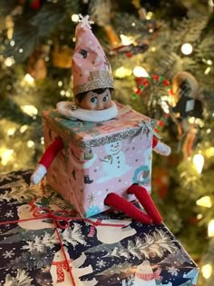 an elf sitting on top of a present under a christmas tree