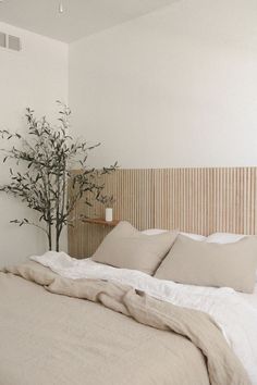 a bed with white sheets and pillows next to a plant