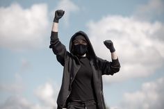 a person wearing a black mask and holding up their hands in the air with one fist raised