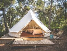 a tent with a bed in it sitting on top of a wooden platform surrounded by trees