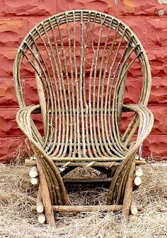 a wicker chair sitting in front of a red brick wall with hay on the ground