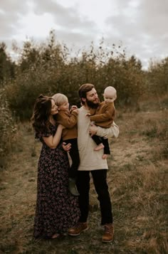 a man and woman holding two children in an apple orchard with the sky behind them