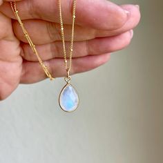 Rainbow Moonstone Necklace, June Birthstone, White Teardrop Pendant on Satellite Ball Layering Chain in Gold or Silver, Dainty Gift for her This simple stunning gemstone necklace features a gorgeous blue flash faceted teardrop bezeled stone in 14k Gold Filled or Sterling Silver. The white moonstone pendant is suspended from a minimalist satellite ball chain in the finish of your choice. This necklace is simple, elegant and just perfect for layering or to wear on its own. It make a great bridesmaid necklace. This Boho Necklace will turn heads at any of your social events. Please note that the blue flashes in the stones may vary from pendant to pendant, but they are all very similar to one another.  About this Necklace: - Gemstone: Blue flash Rainbow Moonstone - Birthstone: June - Moonstone