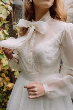 a mannequin wearing a white dress with a bow around the neck and long sleeves