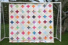 a quilt hanging on a fence in front of some trees and grass with an iron gate behind it