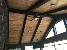 a ceiling fan in the middle of a room with wood paneling and large windows