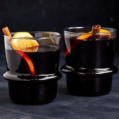 two glasses filled with black liquid and orange peels on top of each glass, sitting on a table