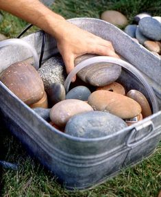 a bucket filled with lots of rocks sitting on top of a grass covered field next to a person's hand