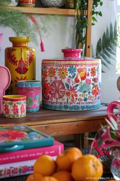 a table topped with lots of colorful vases next to oranges and other items