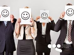 four business people holding up faces with smiley faces drawn on them in front of their faces