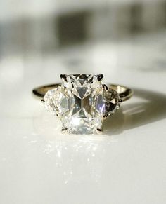 three stone diamond ring sitting on top of a white surface with light shining through it