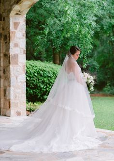 a woman in a wedding dress looking at her veil while she stands under an archway