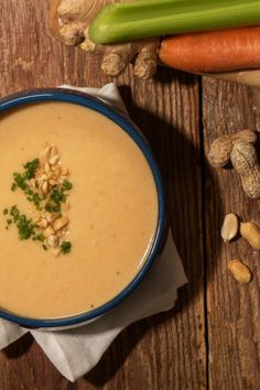 a blue bowl filled with soup sitting on top of a wooden table next to carrots and celery