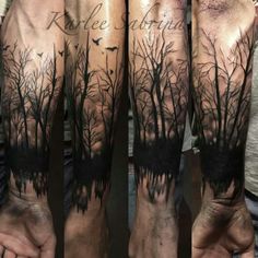 the arm is covered in black and grey ink with trees on it, while birds are flying