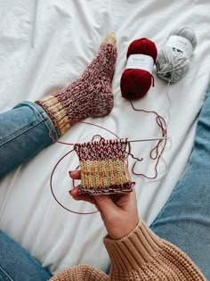 a woman is knitting on the bed with her feet propped up next to some crocheted items