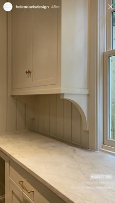 an empty kitchen with white cabinets and marble counter tops in front of a large window