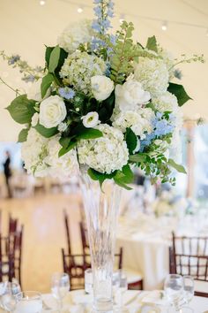 a tall vase filled with white and blue flowers on top of a dining room table