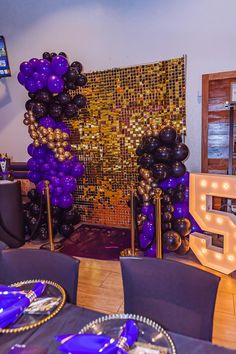 a party room with purple and black balloons on the wall, gold foiled letters and lights