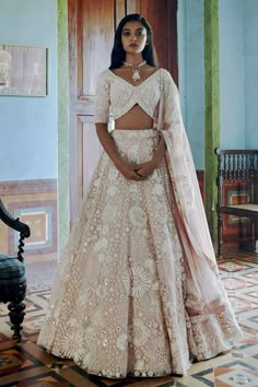 a woman in a white and pink lehenga standing on a tiled floor with a chair