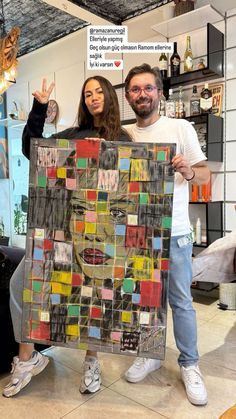 two people standing next to each other holding up a large piece of art made out of squares