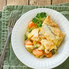 a white plate topped with chicken pot pie and veggies next to a fork