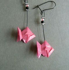 two pink origami fish earrings hanging from black hooks on a gray surface with beads