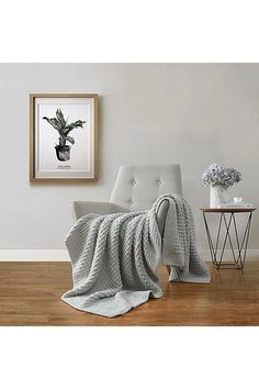 a chair with a blanket on it next to a table and flowers in a vase