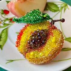 there is a piece of fruit made out of glass beads on a white plate with green leaves