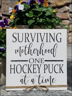 a sign that says surviving motherhood one hockey puck at a time with flowers in the background