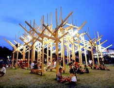 people sitting on the ground in front of wooden structures at an outdoor event with lights