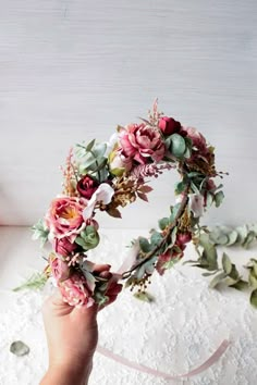 a hand holding a flower crown on top of a white surface with pink and green flowers