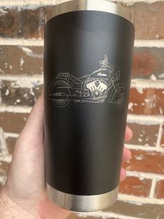 a hand holding a black and silver cup with a drawing of a motorcycle on it