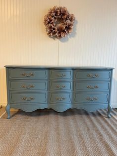 a blue dresser sitting on top of a carpeted floor next to a wreath hanging on the wall