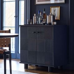 a black cabinet with bottles and glasses on top in a room next to a table