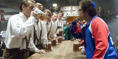 a group of men standing around a wooden table drinking from mugs filled with beer