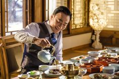 a man pouring tea at a table full of plates and bowls with food on them