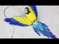 a beaded parrot is hanging from a hoop on a white surface with blue and yellow beads