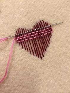 a heart shaped piece of yarn is being stitched on the floor with a needle