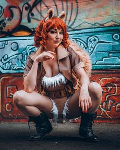 a woman with red hair is sitting on the ground in front of a graffiti wall