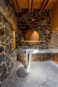 a bathroom with stone walls and a round mirror on the wall next to an oval sink