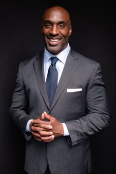 a man in a suit and tie posing for the camera with his hands folded up