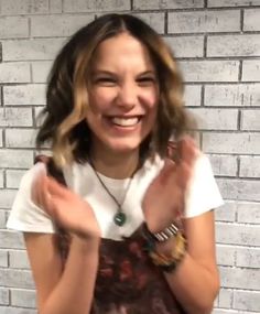 a woman standing in front of a brick wall holding her hands up to the camera