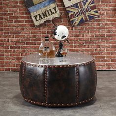 a round leather ottoman sitting in front of a brick wall with two bottles on it