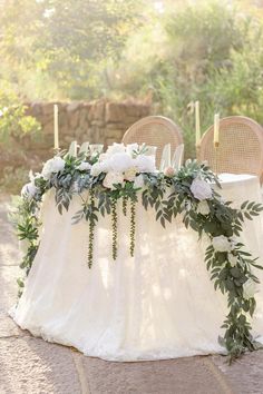 a table with flowers and greenery is set up for an outdoor wedding reception in the sun