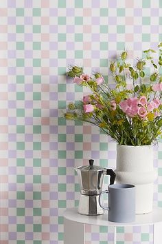 a vase with pink flowers on a table next to a coffee maker and wallpaper