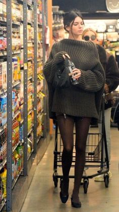 a woman walking down a grocery aisle holding a bottle