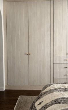 a bedroom with white cupboards and a striped blanket on the bed in front of it