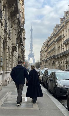 two people walking down the sidewalk in front of cars