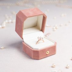 an open ring box sitting on top of a white tablecloth with pearls all around it